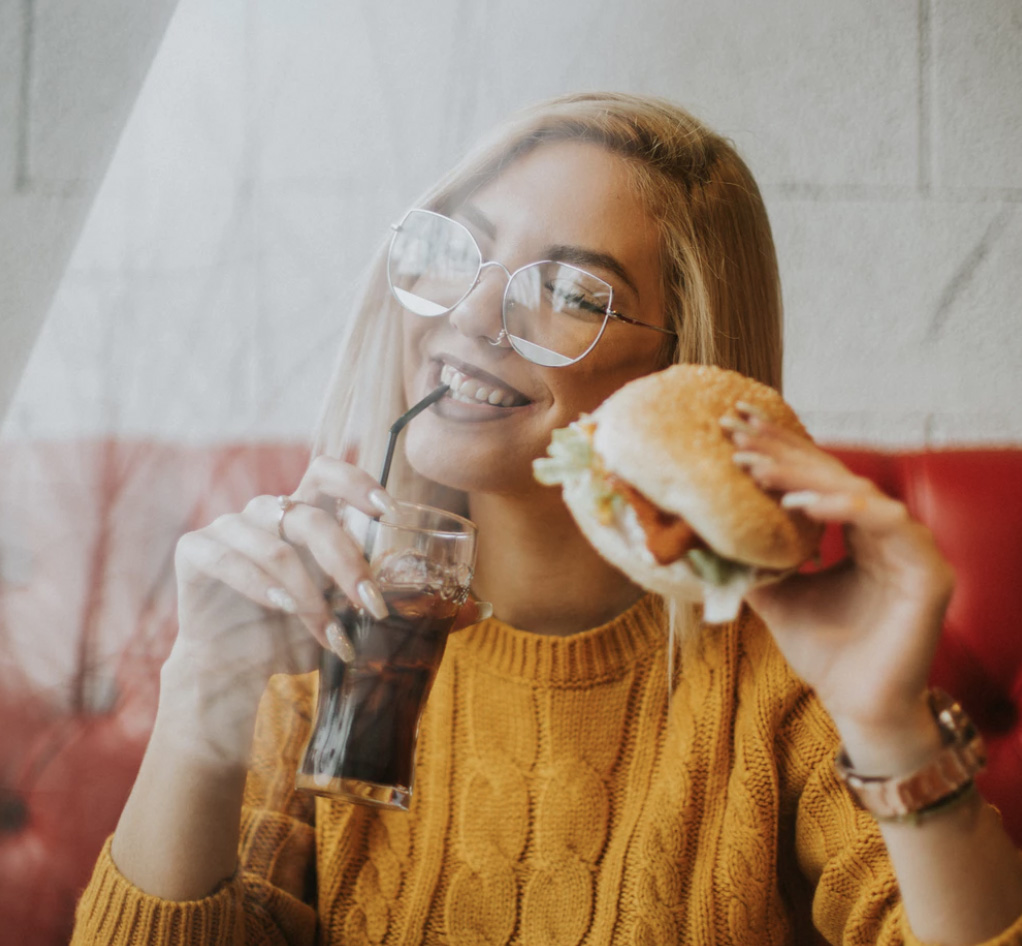 A girl enjoying a soda and her hamburger